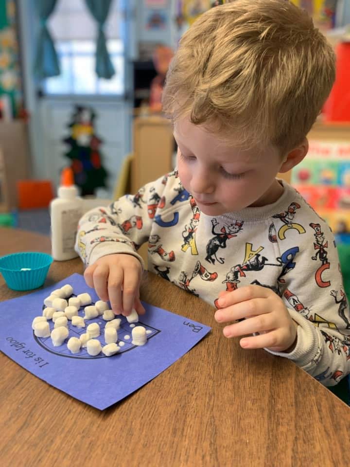 Child placing small white objects on a blue paper with a drawing