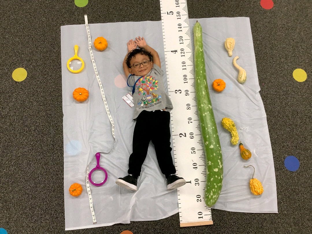 Child lying on a mat next to a large ruler and a long gourd