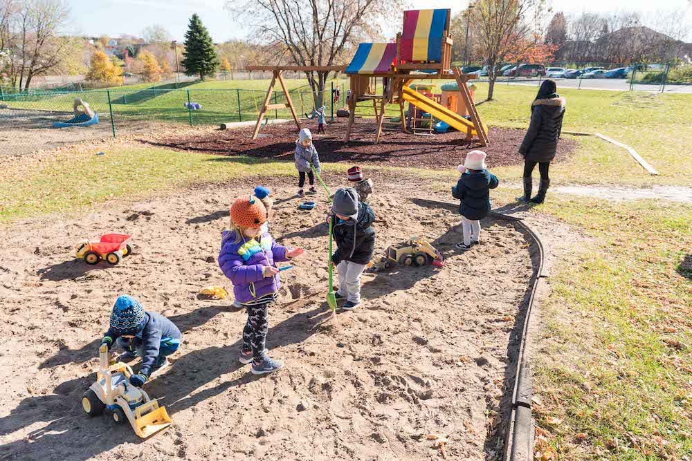 Children playing in a sandbox with toys and a playground in the background