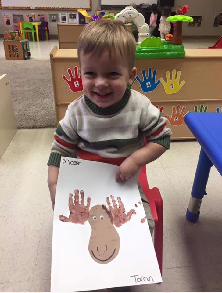 Child holding up a drawing of a moose made with handprints