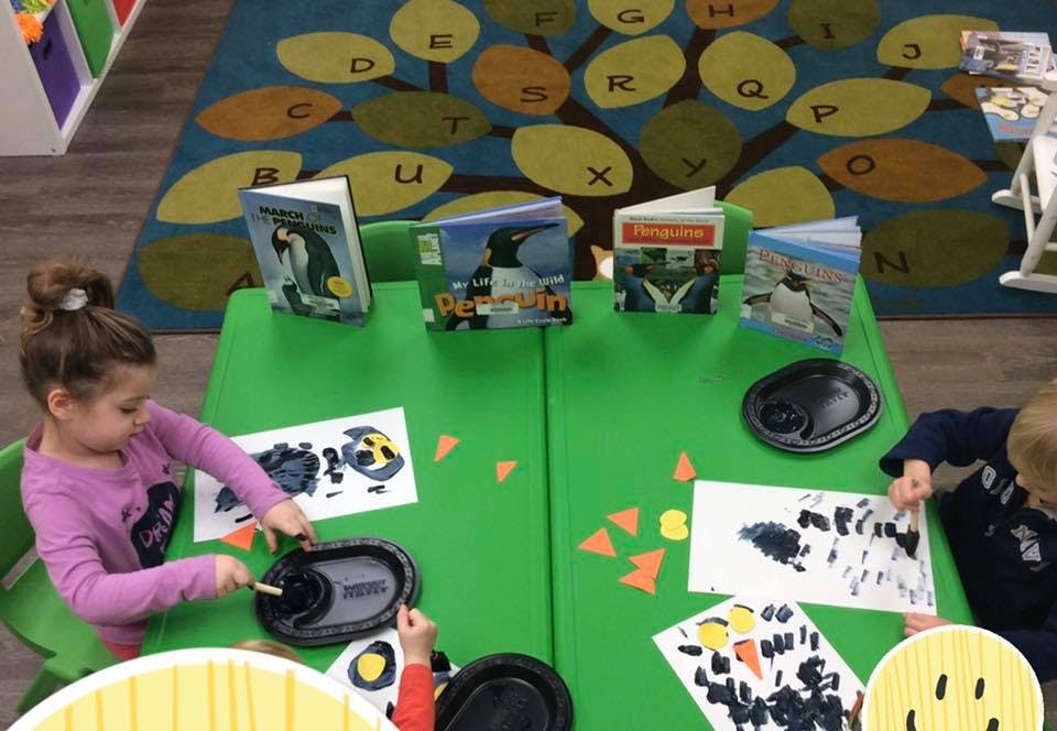 Children painting at a green table in a classroom