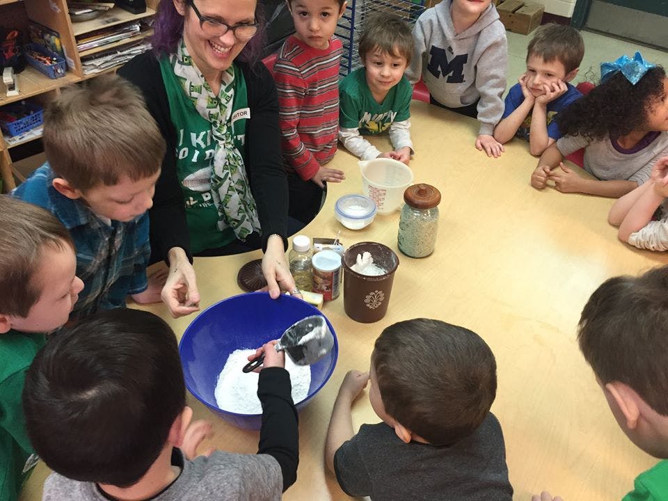 Person and children gathered around a table with a bowl and ingredients