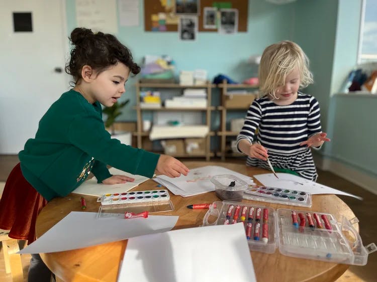 Two children painting and drawing at a round wooden table