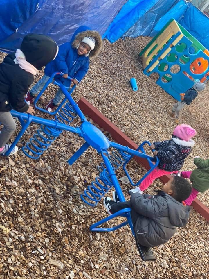 Children playing on a blue seesaw on a wood chip playground