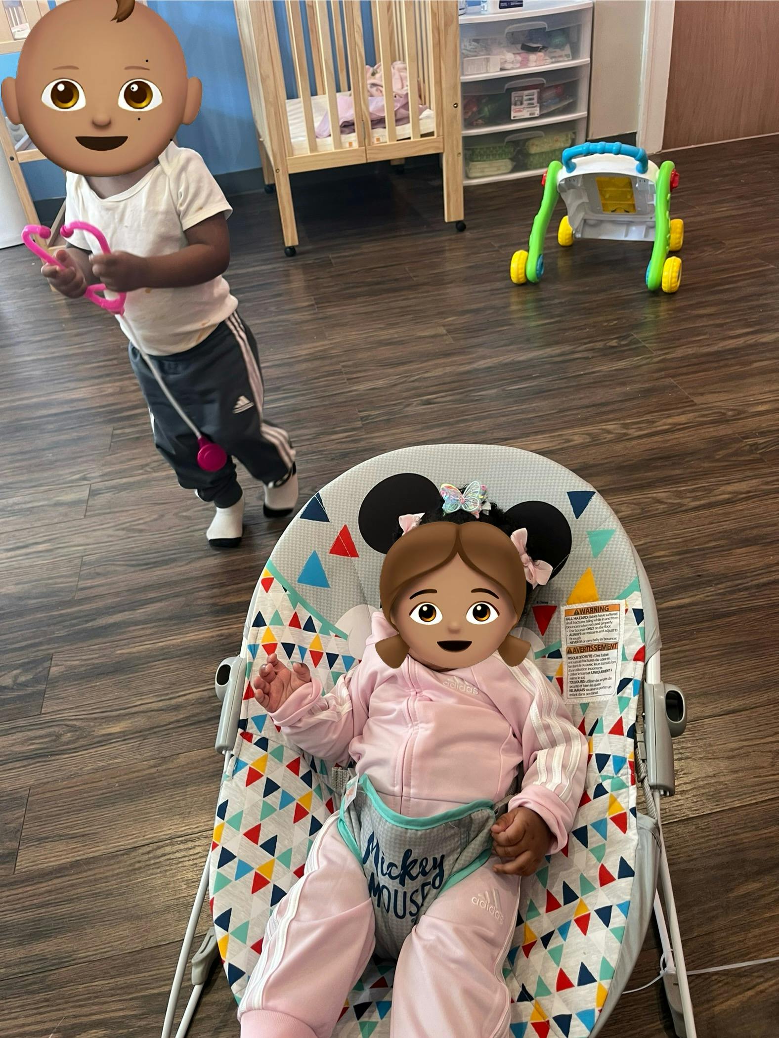 Child standing with a toy and a child in a bouncer