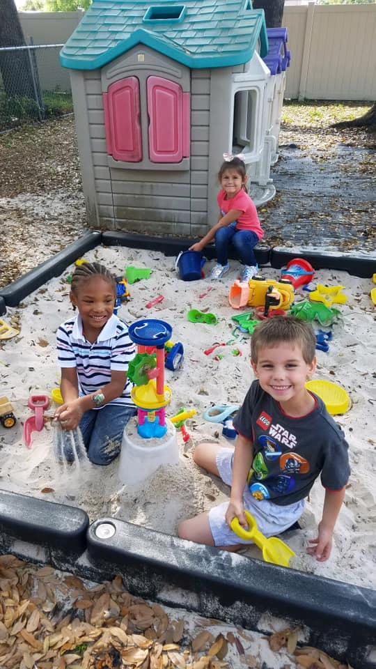 Three children playing in a sandbox with toys
