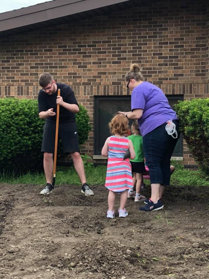 Person with shovel and two children with an adult in a garden