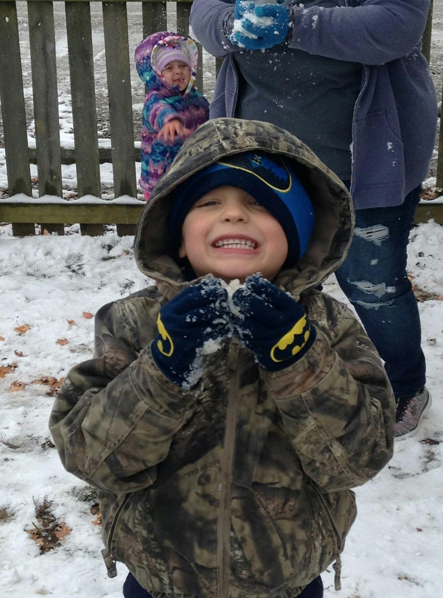 Child in a camouflage jacket and blue hat holding snow in gloved hands