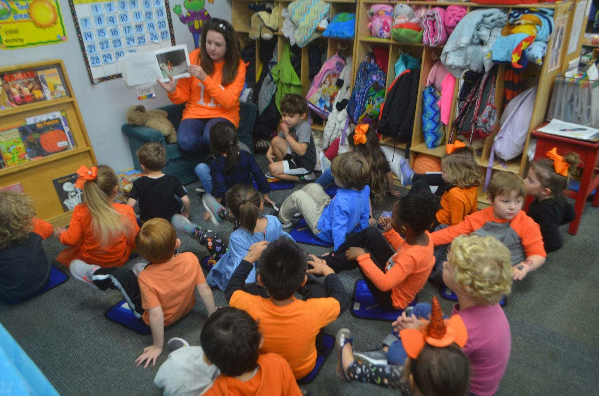 Adult reading a book to a group of children in a classroom