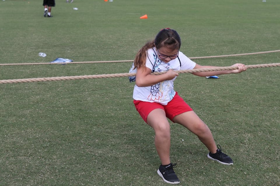 Child pulling a rope during a tug-of-war game on a grassy field