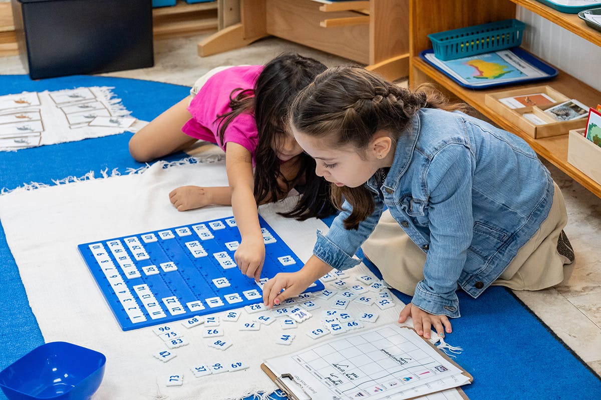 Two children playing with letter tiles on a blue board