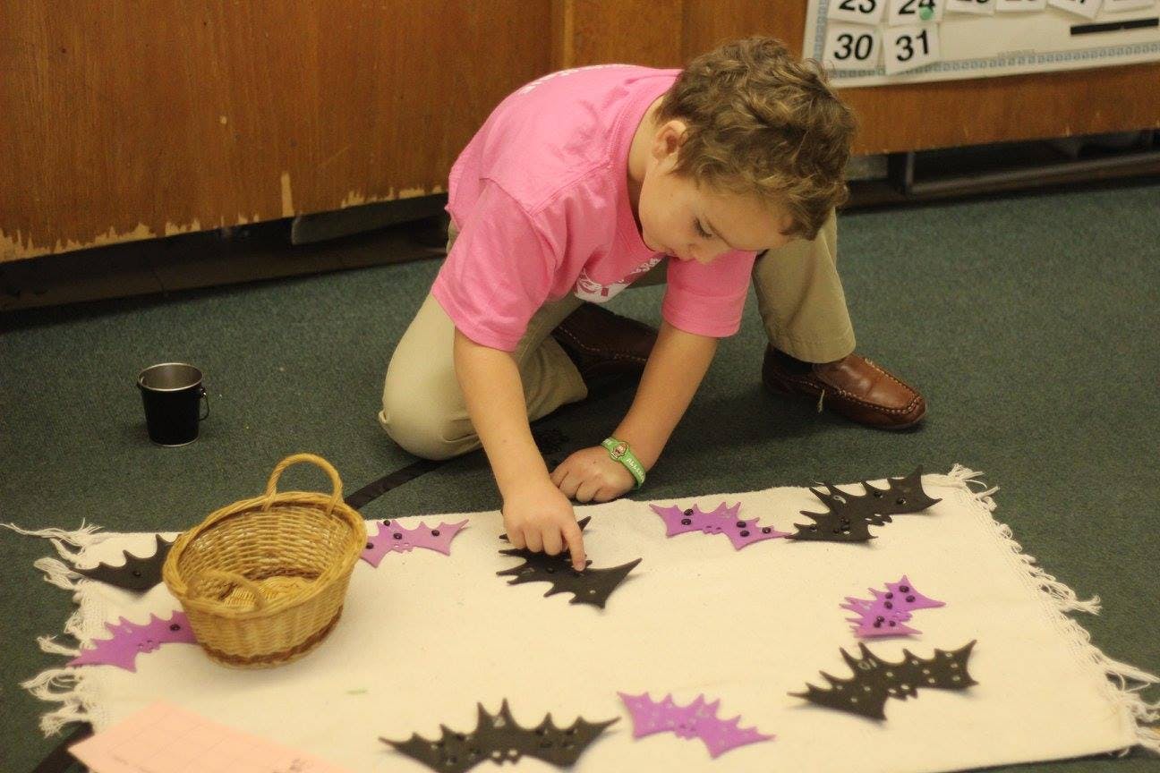 Child kneeling and arranging bat cutouts on a white cloth
