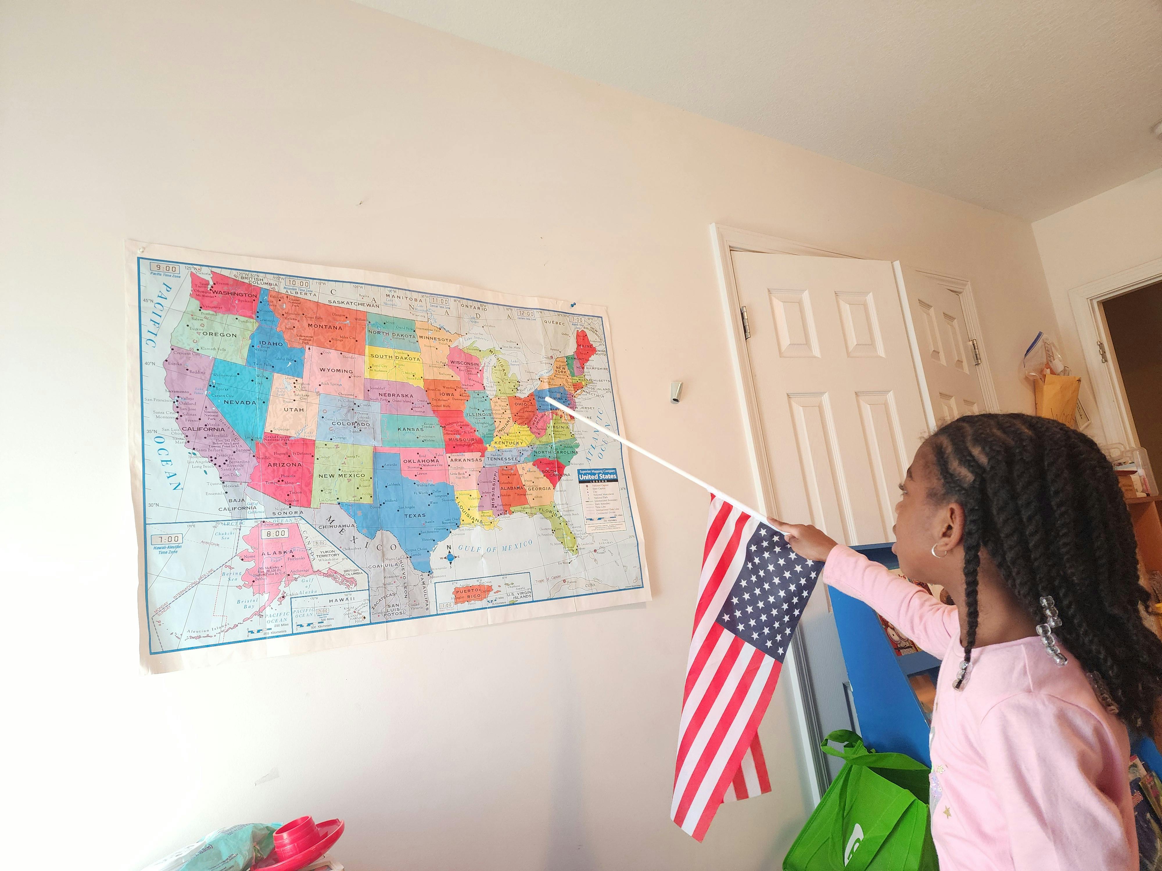 Child holding an American flag on a stick, pointing at a map of the US