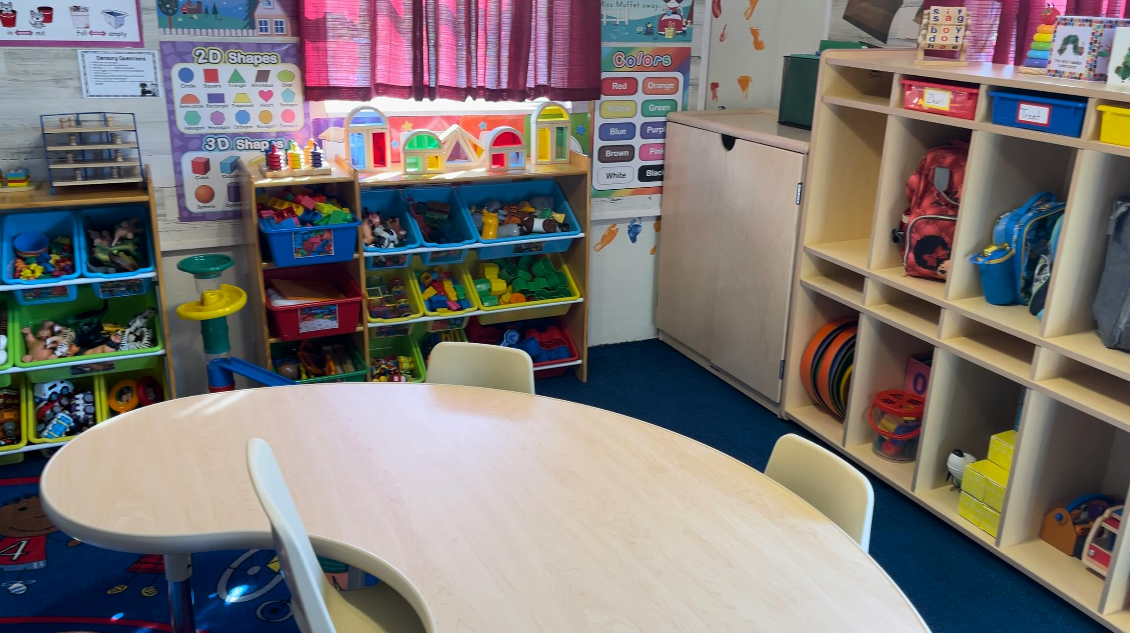 Classroom with tables, chairs, and shelves filled with toys and learning materials
