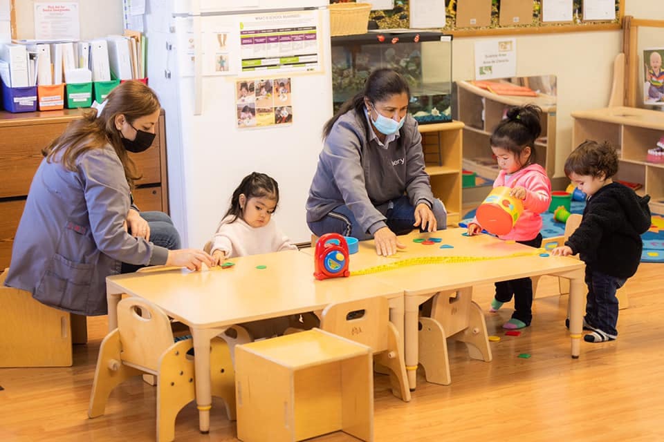 Two people and three children playing with toys at a table