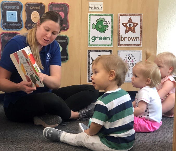 Person reading a book to three children in a classroom