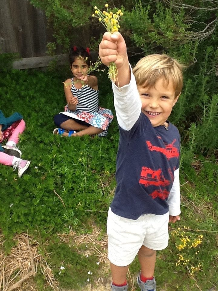 Child holding up a bunch of yellow flowers, another child sitting in the background