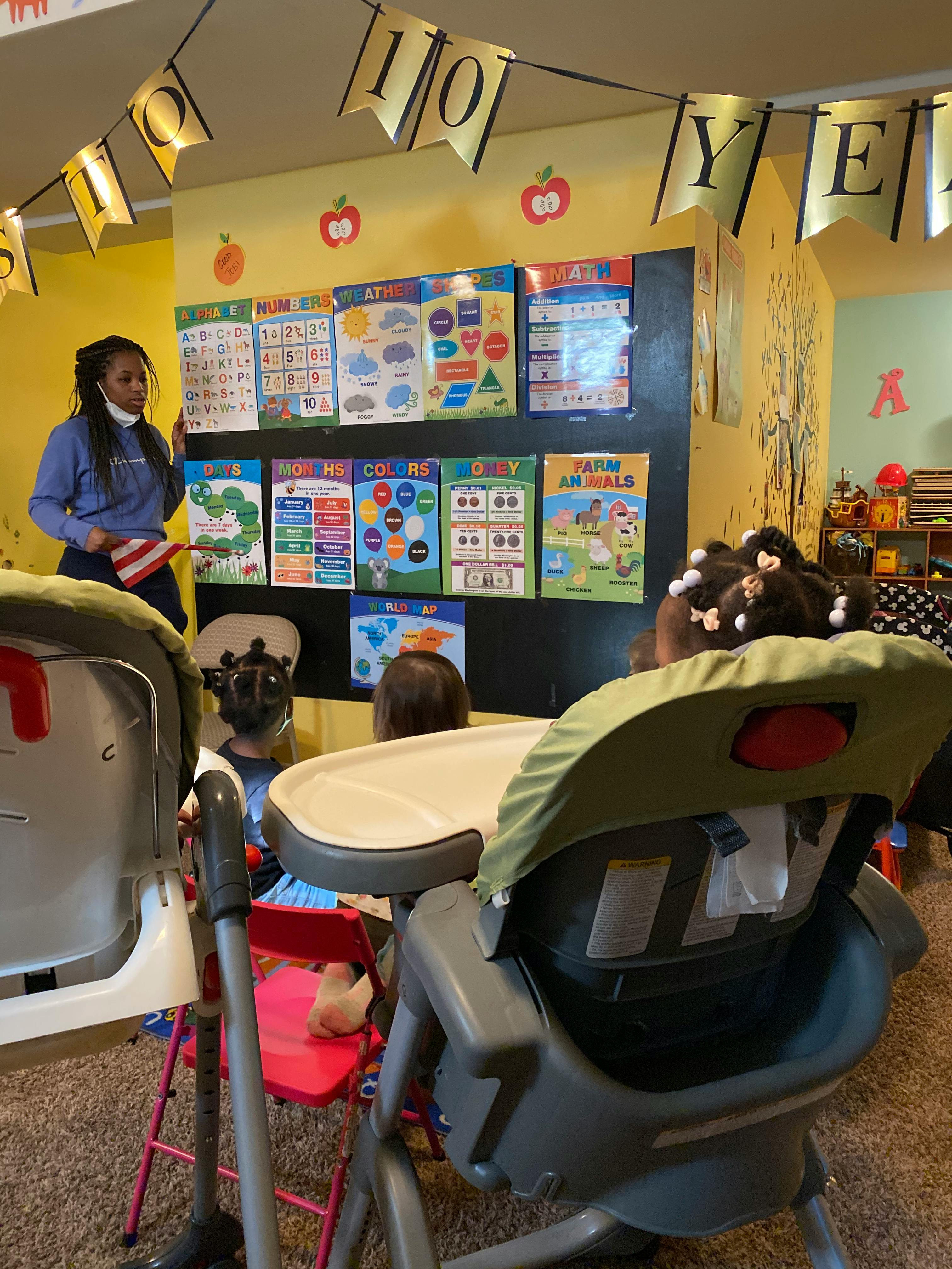 Person standing in front of a wall with educational posters, facing children in high chairs