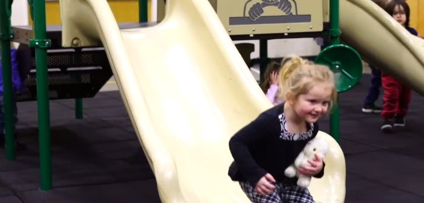 Child on a playground slide holding a stuffed animal