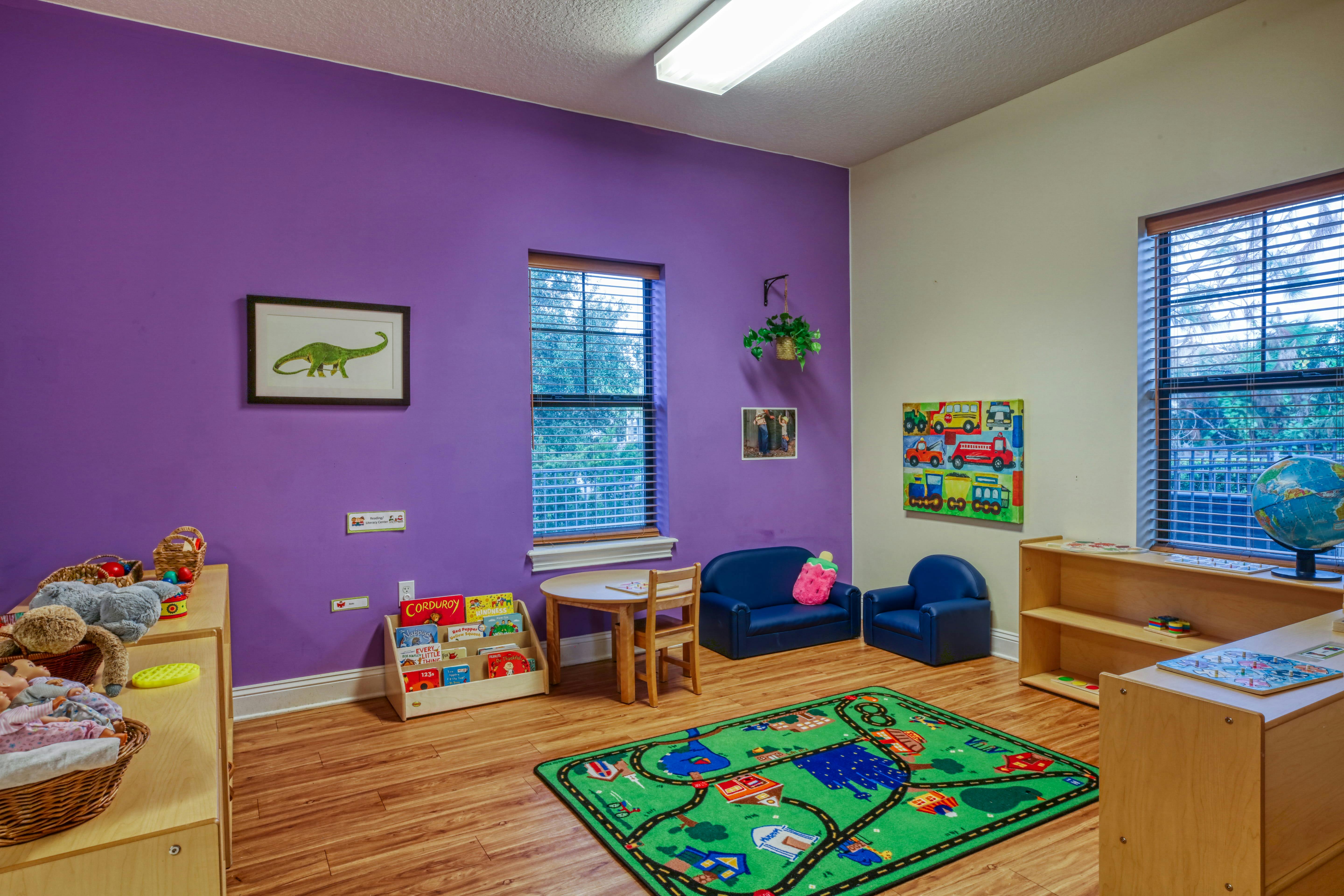 Children's classroom with purple and white walls, small table, chairs, and play rug