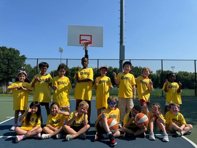 Group of children and teens in yellow shirts posing on a basketball court