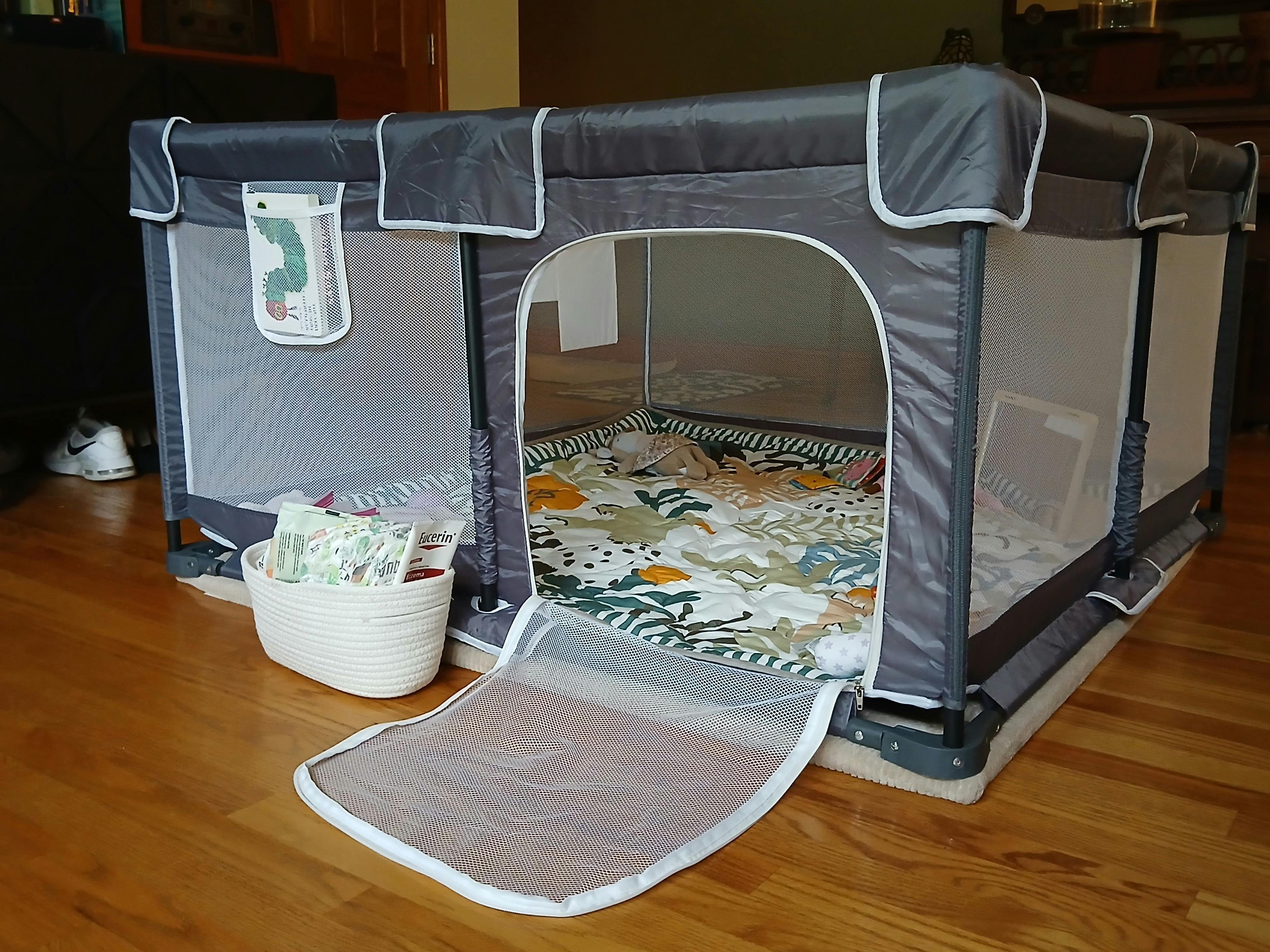 Foldable baby playpen with a mesh door and patterned play mat on a wood floor