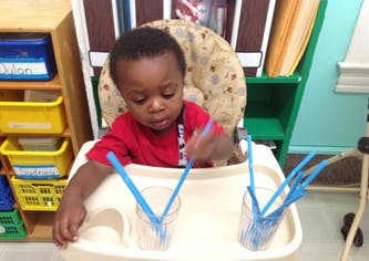 Child in high chair playing with blue plastic forks in cups