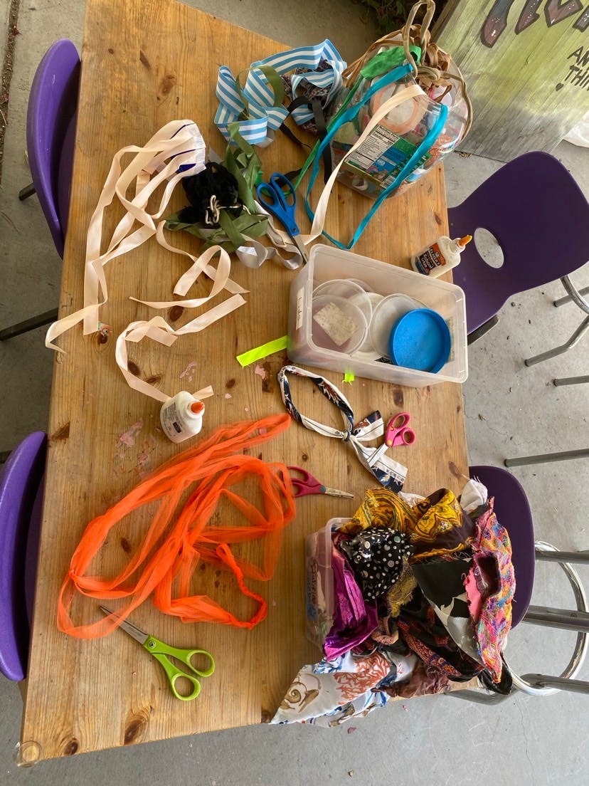 Craft supplies on a wooden table, including ribbons, fabric scraps, glue, and scissors