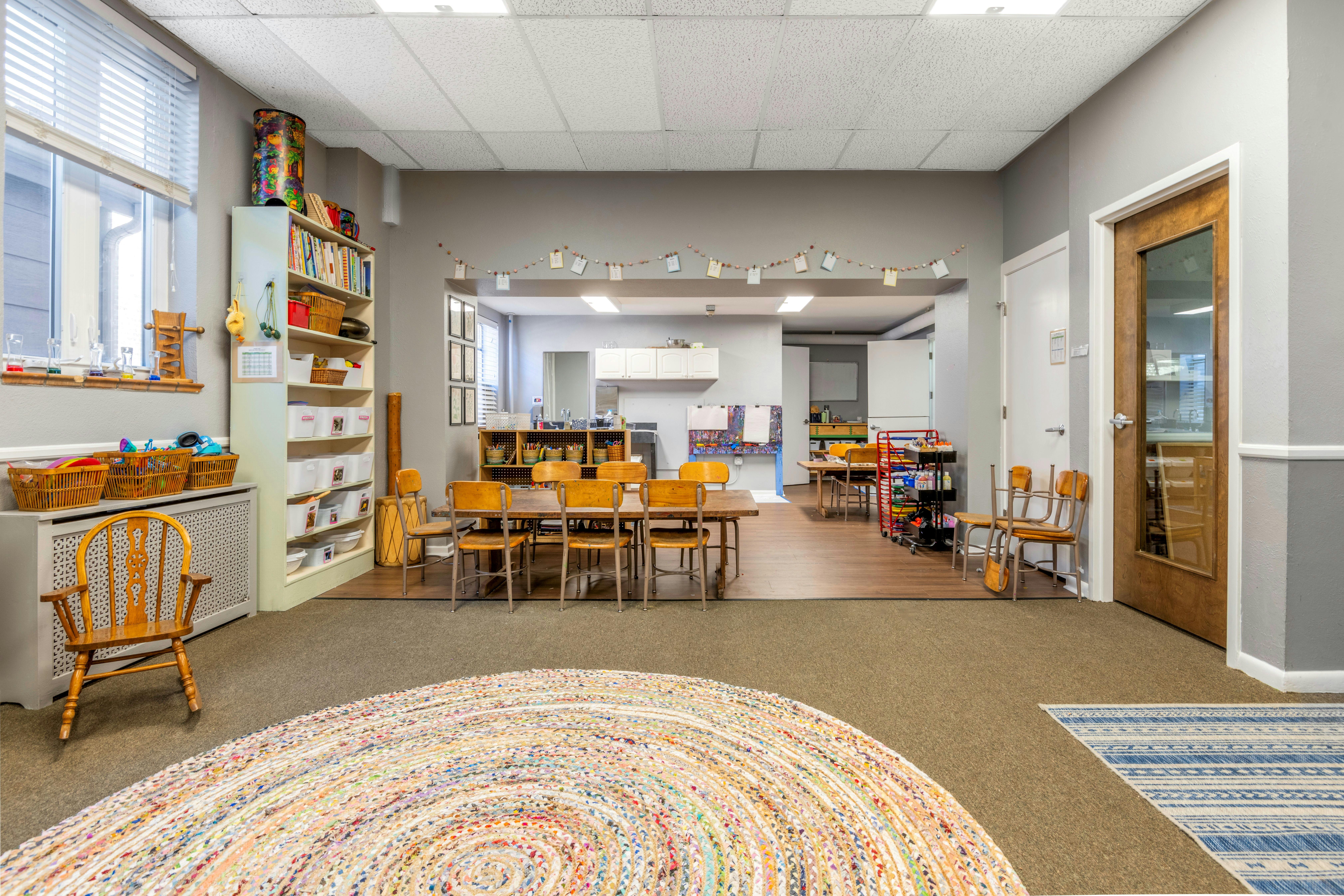 Classroom with small tables and chairs, shelves, and a colorful rug