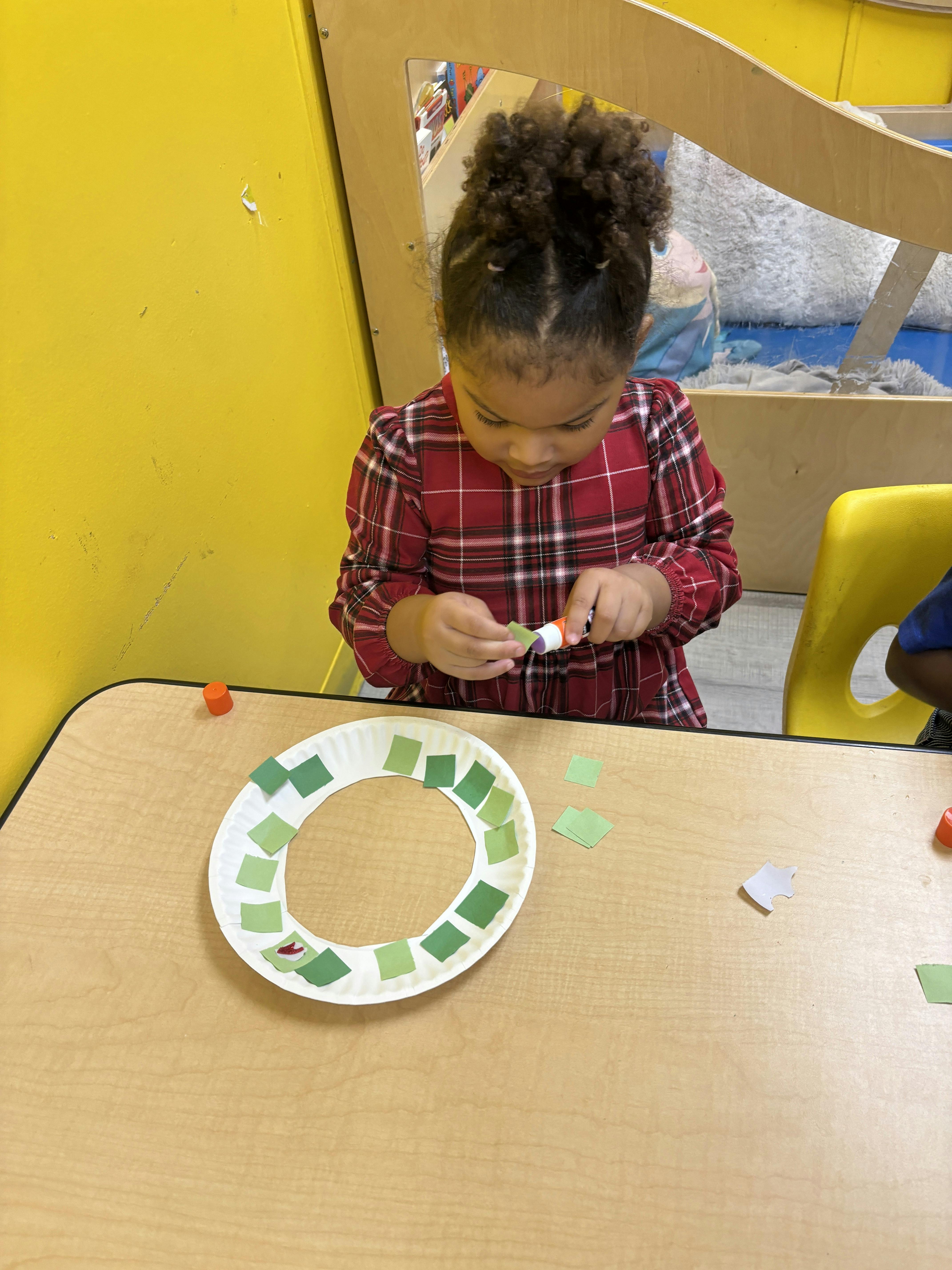 Child gluing paper squares onto a paper plate