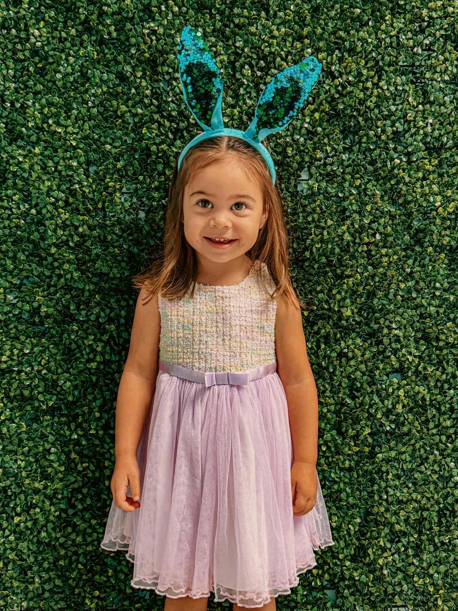 Child wearing bunny ears and a dress standing in front of a green wall