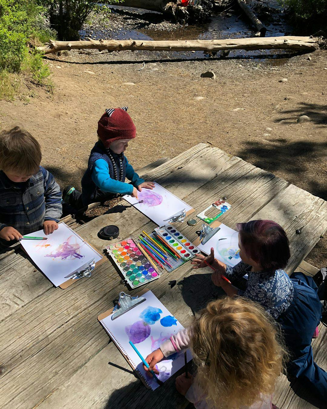 Children painting outdoors at a wooden table