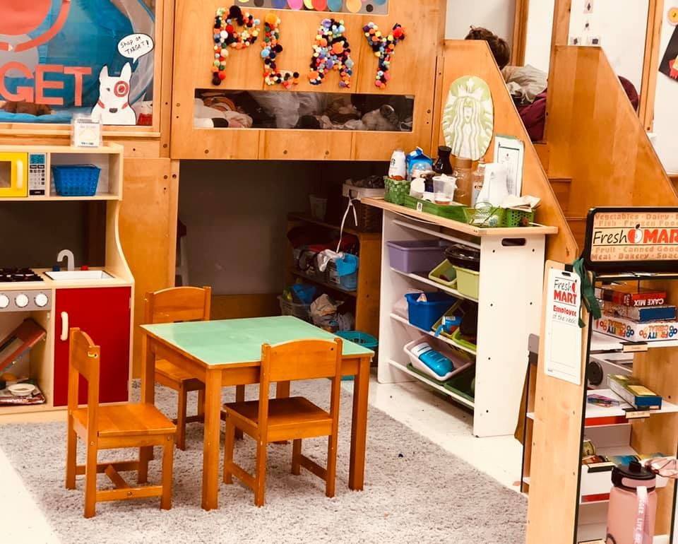 Playroom with small table and chairs, play kitchen, and wooden play structure