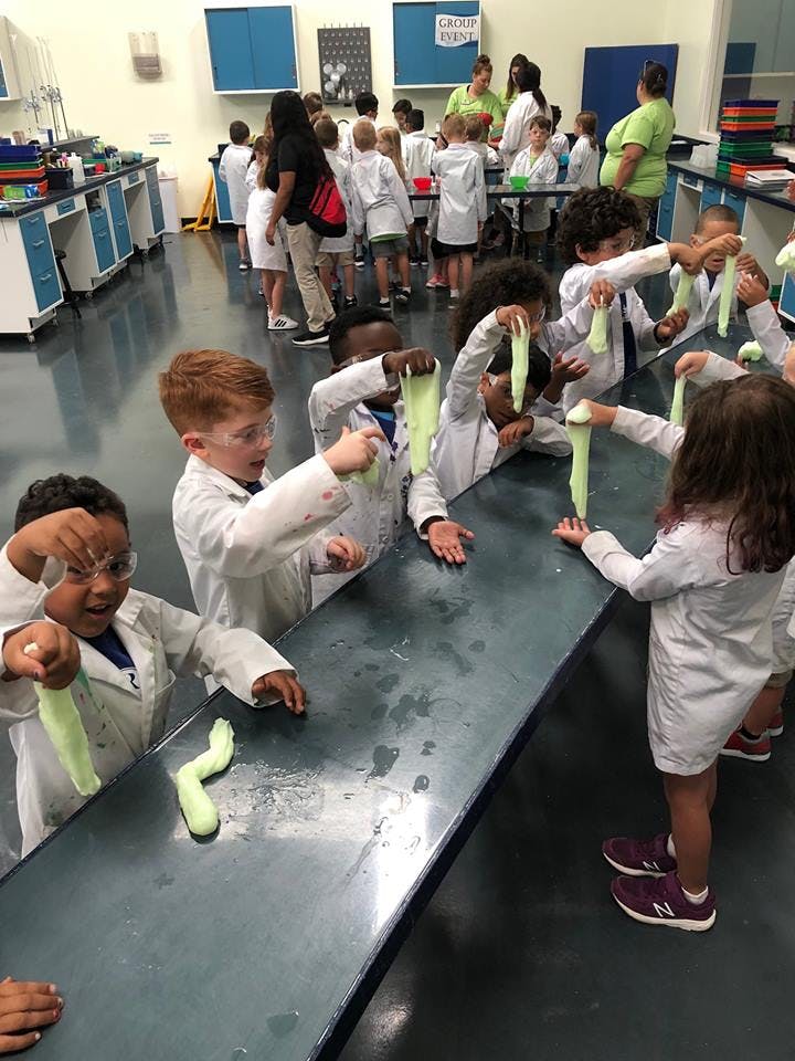 Children in lab coats playing with slime in a classroom