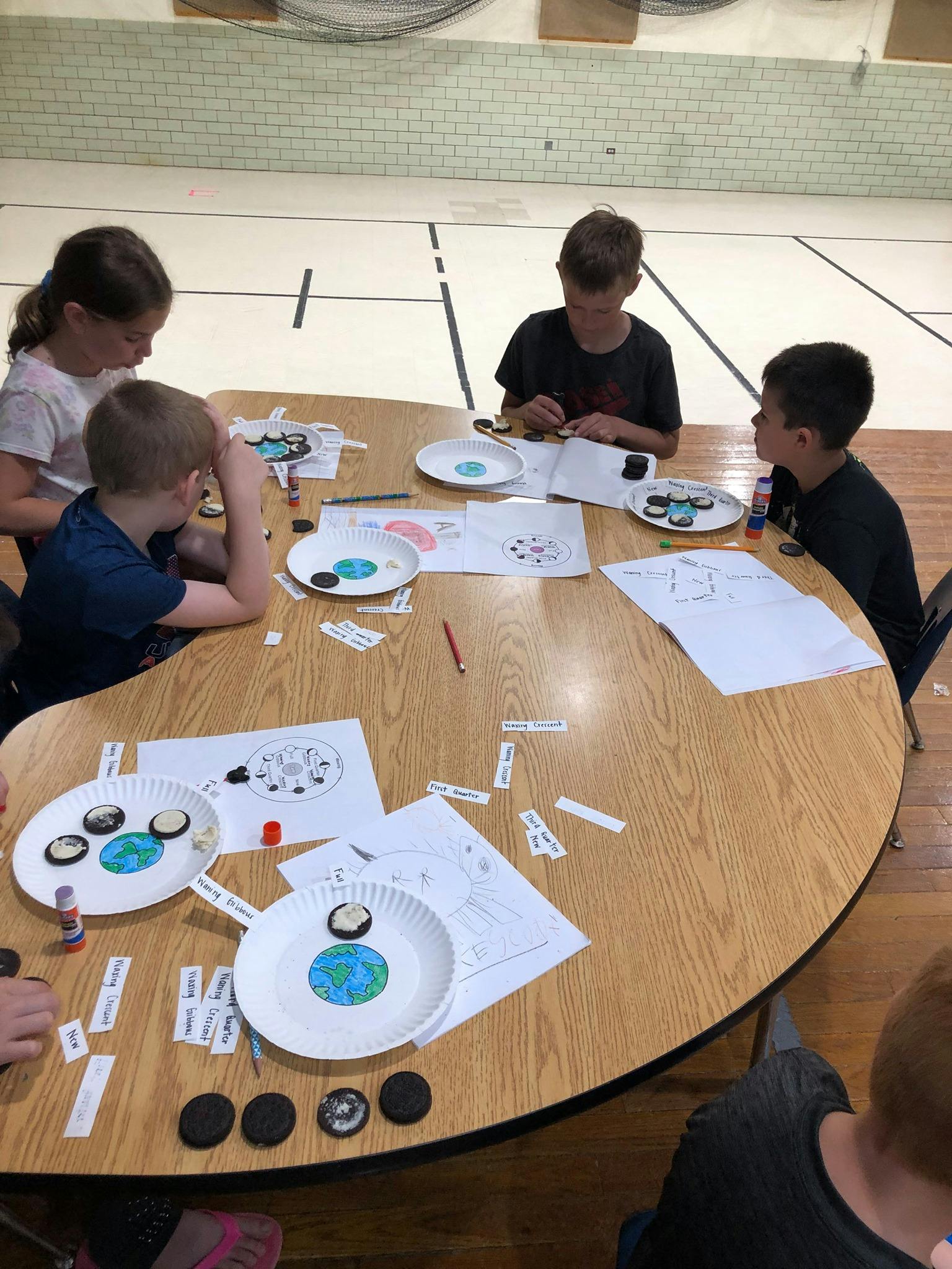 Children at a table doing a craft with paper plates and cookies