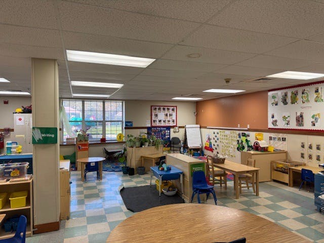 Empty classroom with small tables and chairs, window overlooking a playground