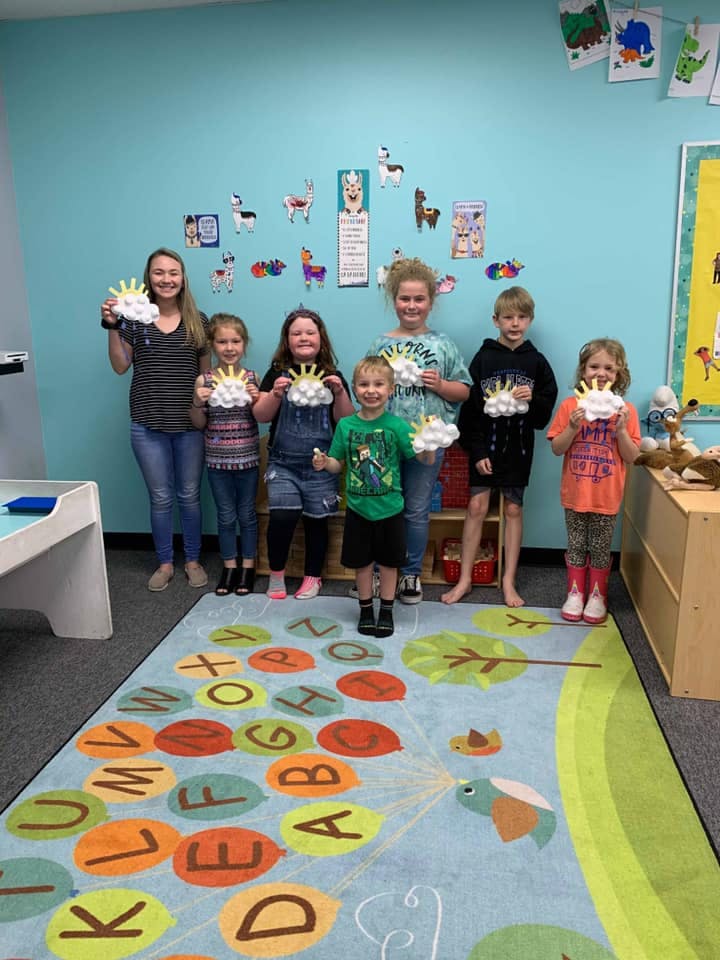Group of children and teens holding sun and cloud crafts in a classroom
