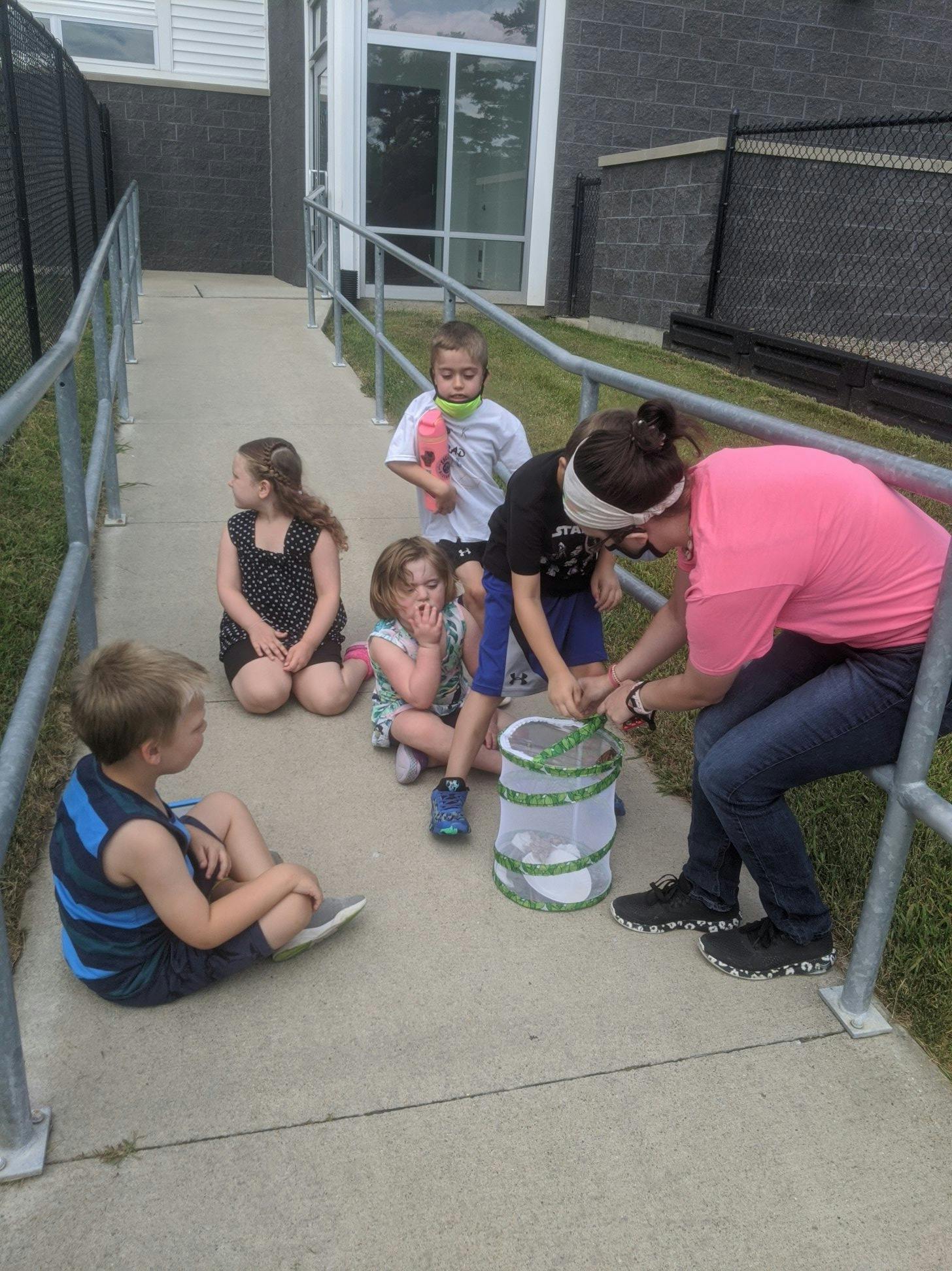 Adult and children gathered around a mesh container on a sidewalk