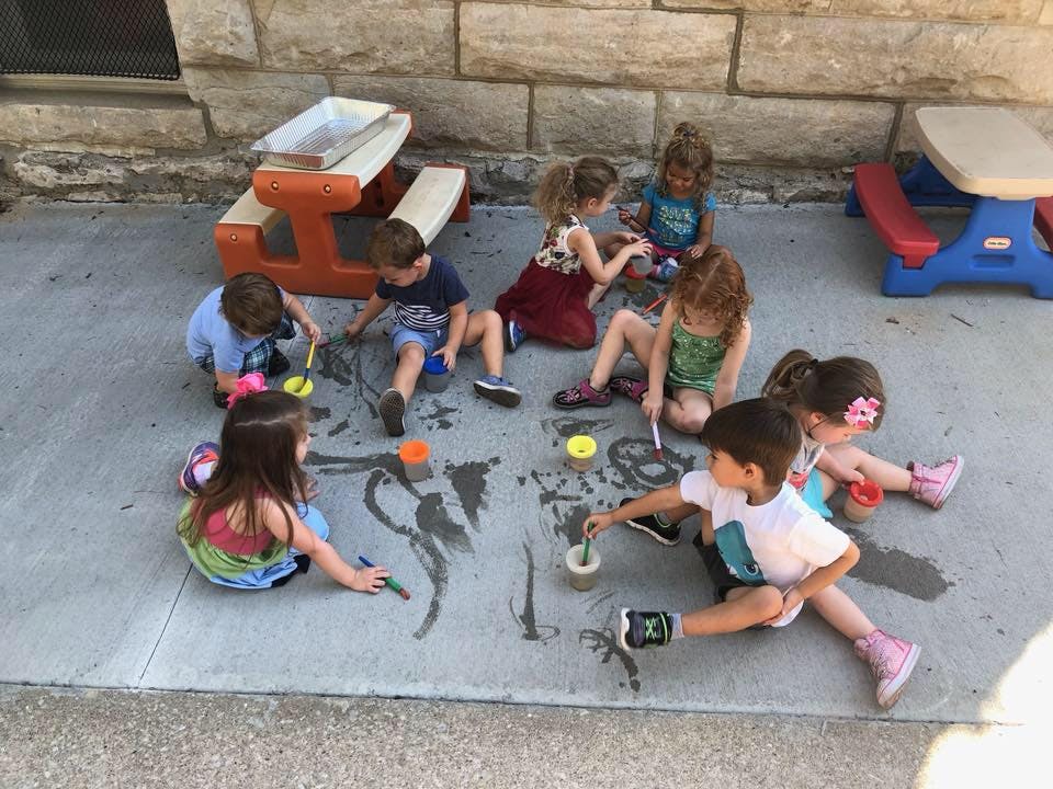 Children sitting on pavement and drawing with water