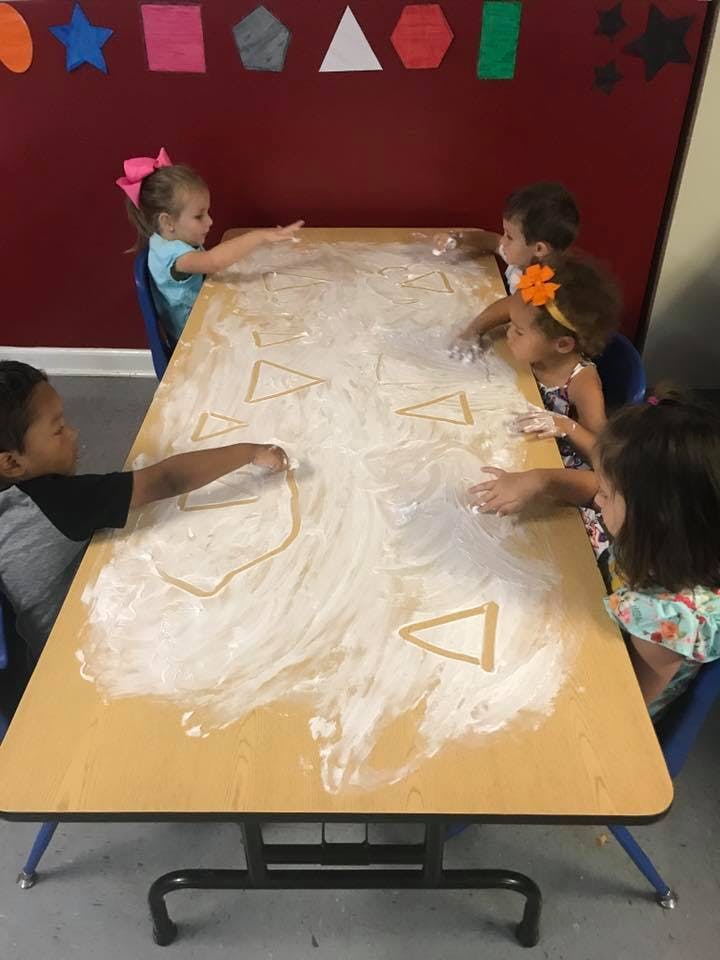 Children playing with flour on a table in a classroom