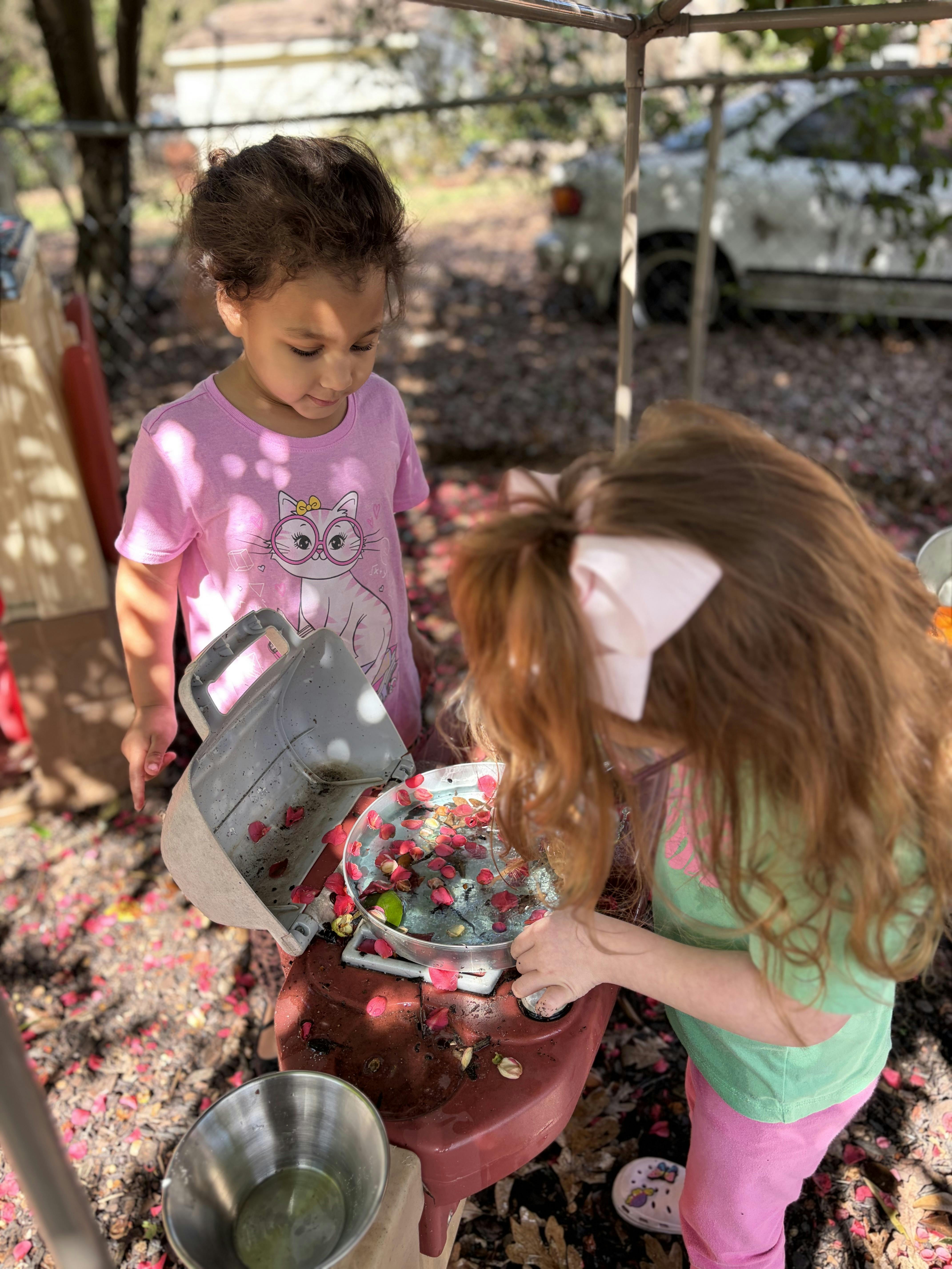 Two children playing with flower petals and water in bowls outdoors