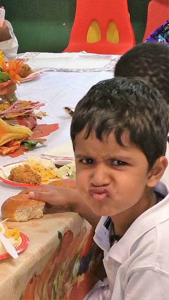 Child making a face while holding a piece of bread at a table with food