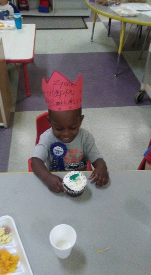 Child wearing a red paper crown and a birthday badge, holding a cupcake