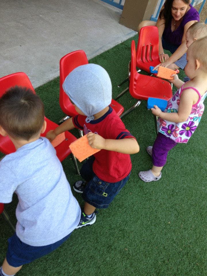 Children playing with paper and red chairs on artificial grass