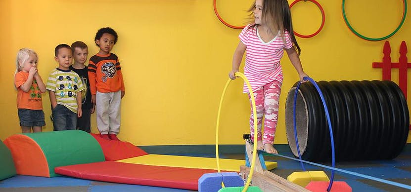 Child balancing on a beam with a hoop, other children watching