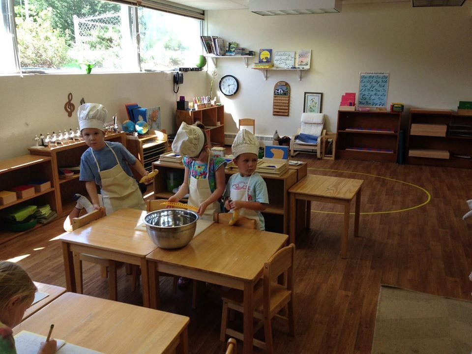 Three children in chef hats and aprons at a table with a mixing bowl