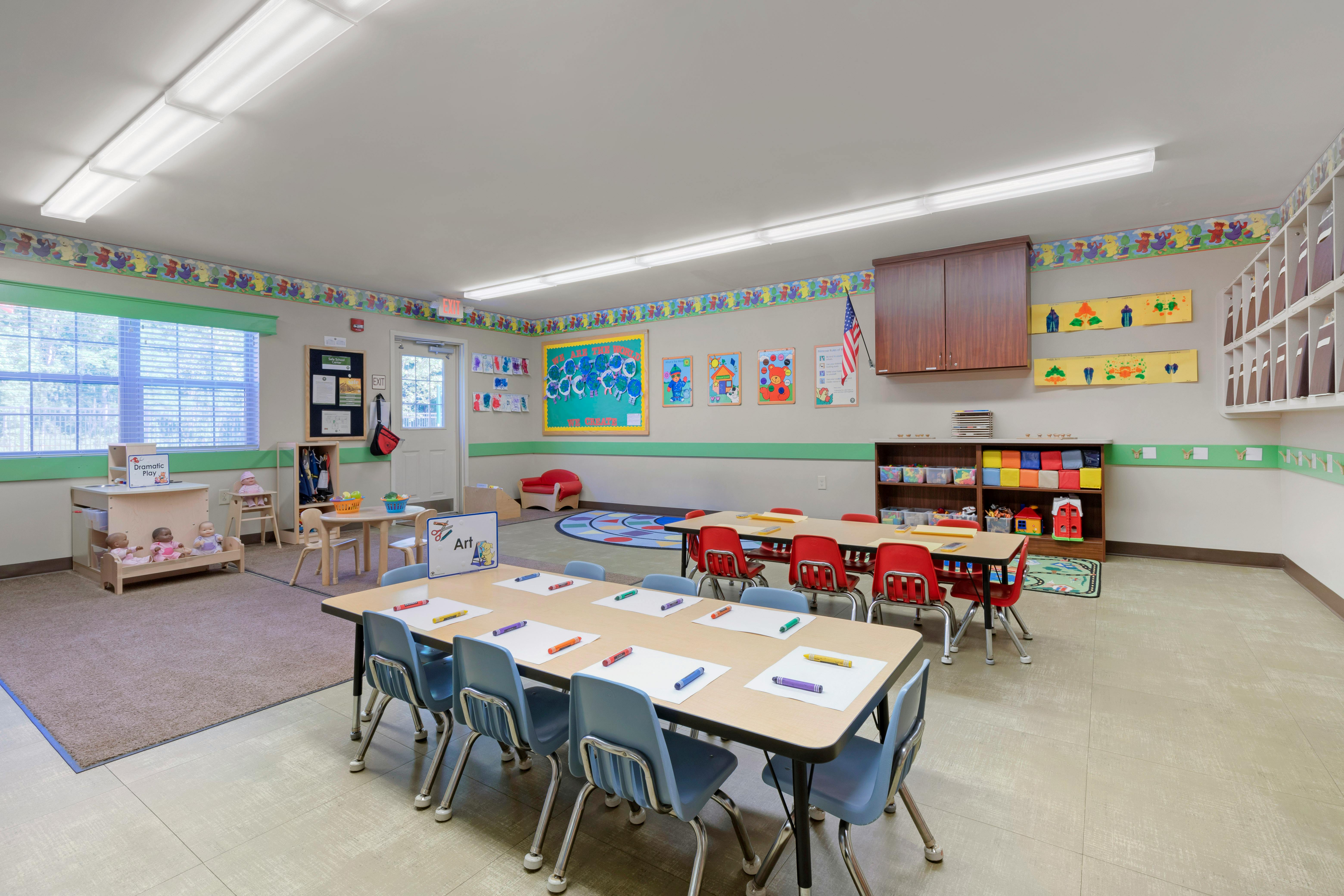 Empty classroom with small tables and chairs, colorful decorations, and toys