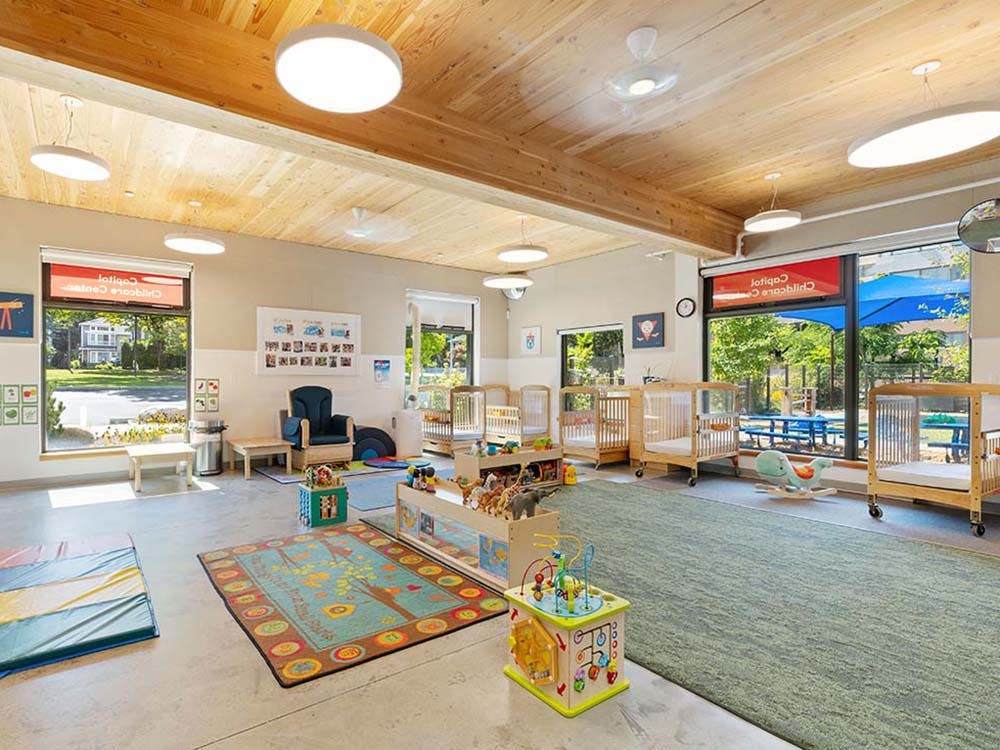 Childcare room with multiple cribs, a play rug, and toys