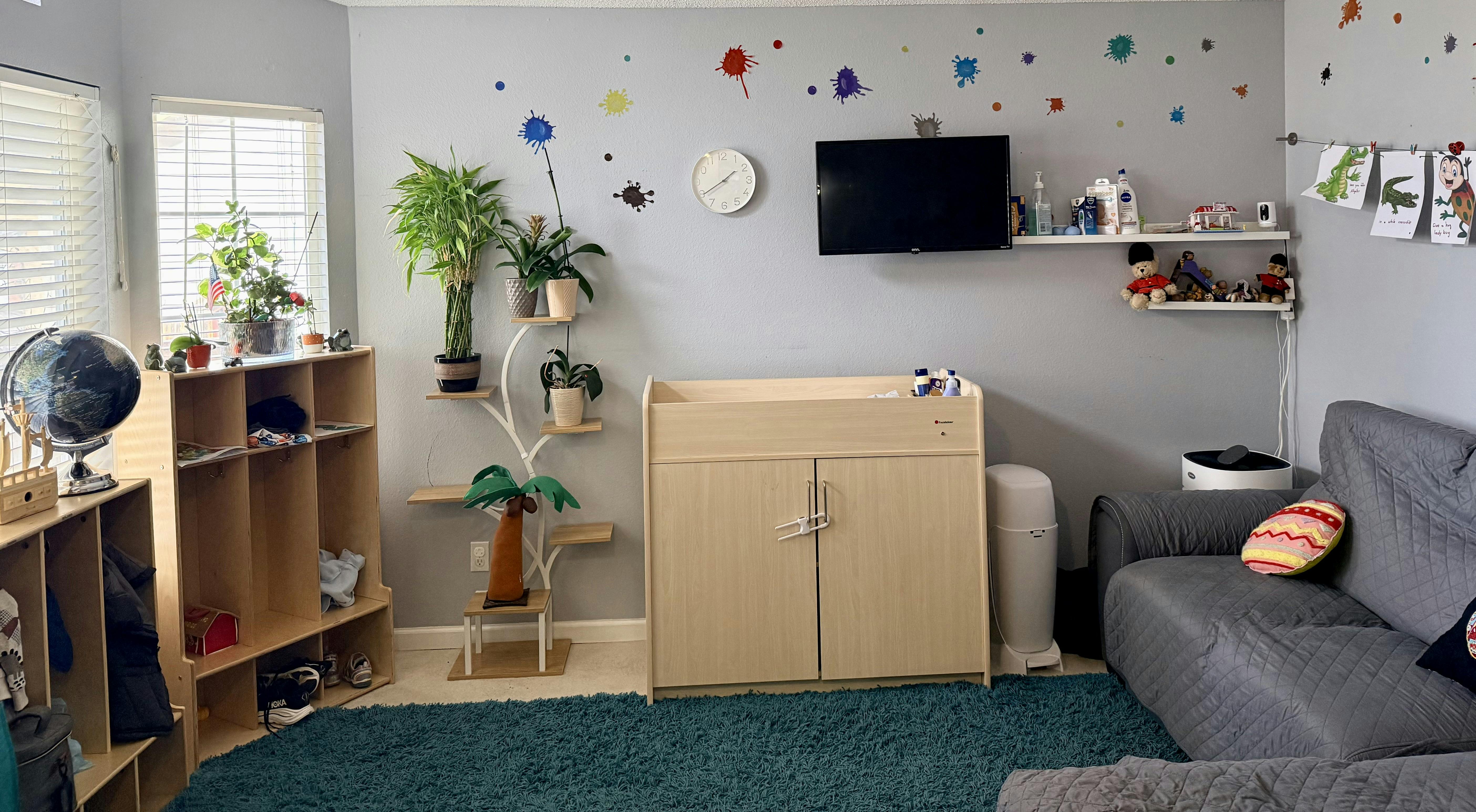 A room with a changing table, shelves, plants, and a sofa with a blue rug