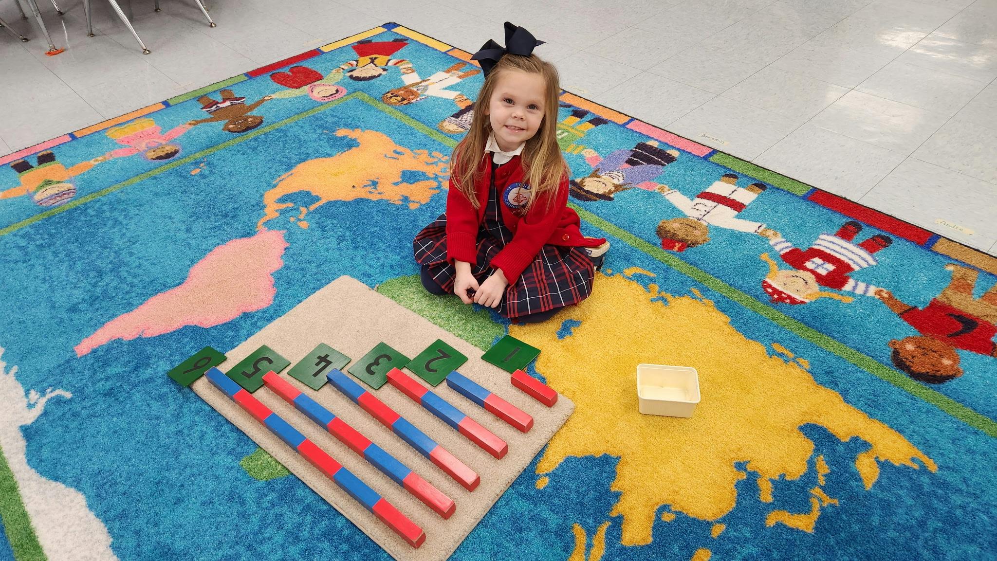 Child sitting on a world map rug with learning materials
